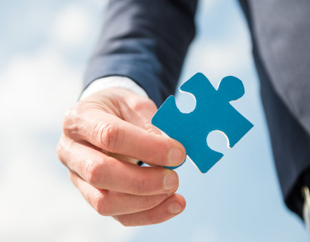 Closeup of hand with jigsaw puzzle. Sky background.の写真素材