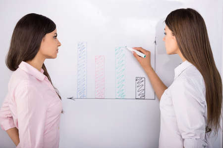 Two beautiful office workers drawing business strategy on flip chart.の写真素材