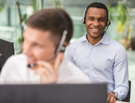 Agent smiling while working on his computer with colleague next to him.