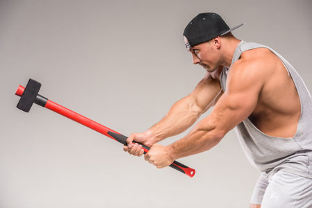 Muscular bodybuilder with hammer on gray background. Sudio shot.