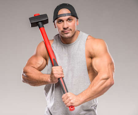 Muscular bodybuilder with hammer on gray background.の写真素材