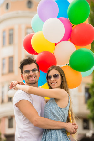 Young couple dressed casual bonding each other and holding bright helium balloons.の写真素材
