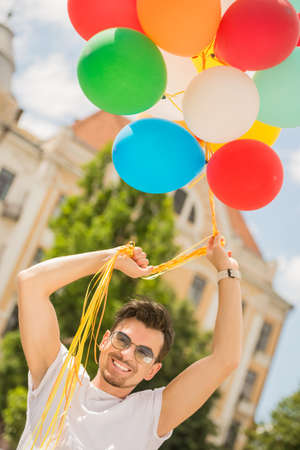 Handsome man holding bunch of colorful balloons outdoors.の写真素材