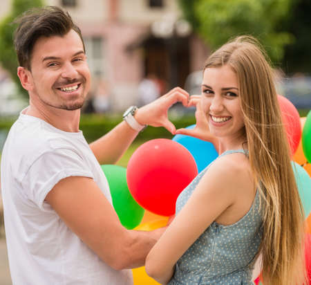 Young lovely couple with balloons shaping heart symbol with hands outdoors.の写真素材