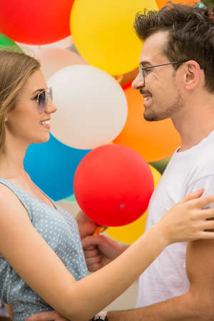 Lovely young couple with colorful balloons looking to each other and smiling. Side view.の写真素材
