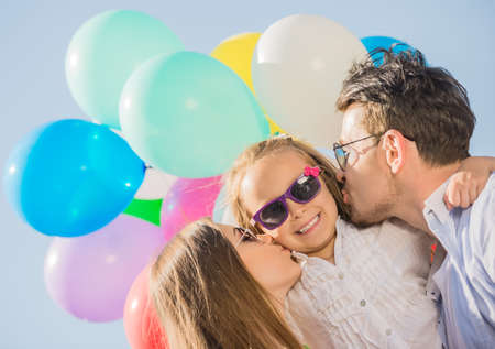 Young attractive parents with balloons kissing their little daughter on the cheek.の写真素材