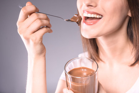 Happy  young woman tasting delicious chocolate paste over gray background. Close-up.の写真素材