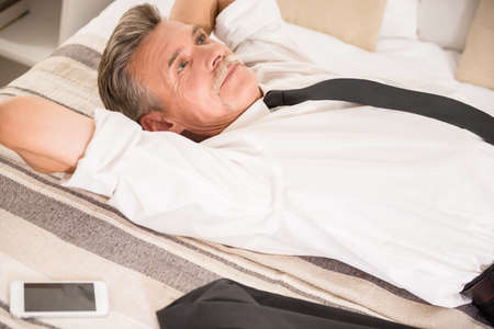 Top view of businessman is lying with his phone on bed and dreaming about something.の写真素材