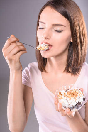 Sweet temptation. Young smiling woman enjoying creamy dessert over gray background.の写真素材