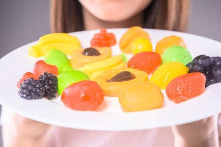 Sweet-tooth. Young woman holding plate with  fruit jellies over gray background. Close-up.の写真素材