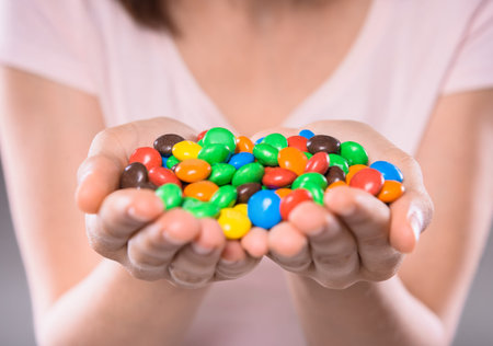 Young woman holding colorful chocolate drops over  gray background. Close-up.