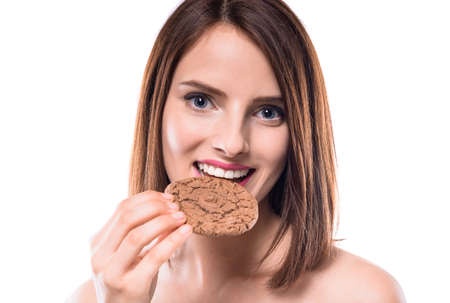 Sweet temptation. Beautiful woman tasting  chocolate biscuit over white background.の写真素材