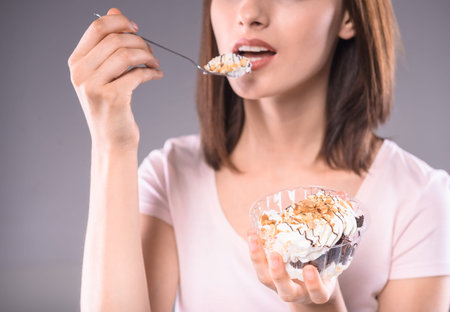 Sweet temptation. Young smiling woman tasting creamy dessert over gray background. Close-up.の写真素材