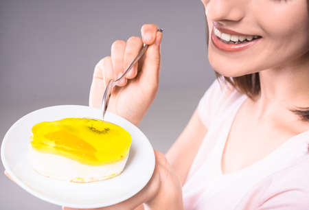 Happy young woman tasting delicious fruit cake over gray background. Close-up.の写真素材