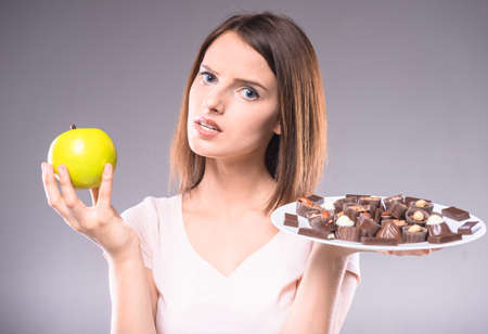Difficult decision. Worried woman choosing between chocolates and  apple. Healthy lifestyle concept.の写真素材
