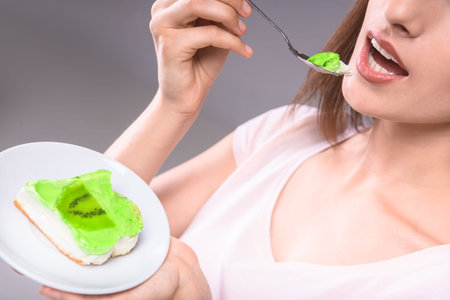 Happy young woman tasting delicious fruit cake over gray background. Close-up.の写真素材