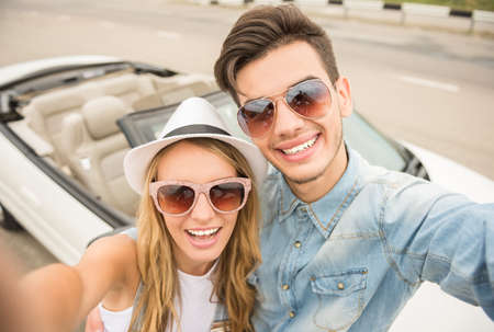 Young cheerful couple in sunglasses taking selfie against cabriolet.の写真素材