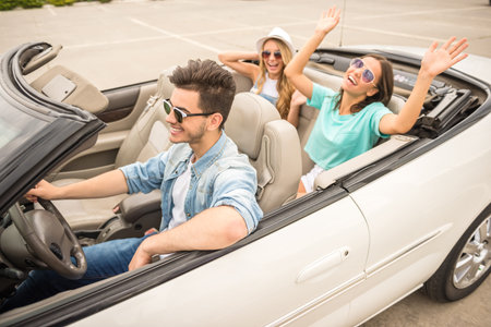 Three happy friends in sunglasses traveling in the cabriolet. Two girls having fun on rear seats.の写真素材
