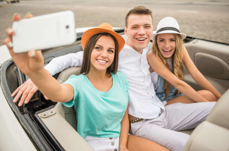 Three beautiful friends taking selfie while sitting in the cabriolet on rear seats.の写真素材