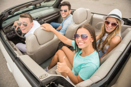 Happy friends in sunglasses sitting on the cabriolet and looking at camera.の写真素材