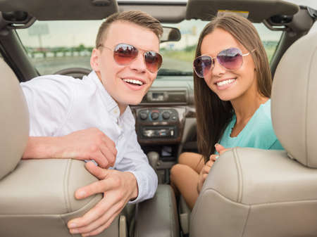 Beautiful couple in sunglasses sittling on the cabriolet and looking at camera. Back view.の写真素材