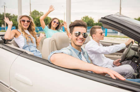 Four happy friends in sunglasses traveling in the cabriolet. Two girls having fun on rear seats.の写真素材