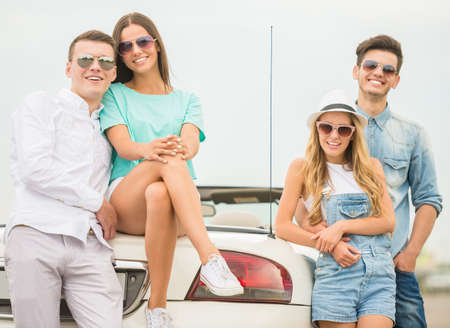 Two young couples in vacation. They are standing near cabriolet, looking at camera and smiling.の写真素材