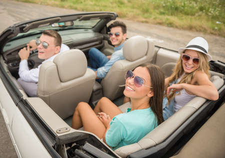Happy friends in sunglasses sitting on the cabriolet and looking away.の写真素材