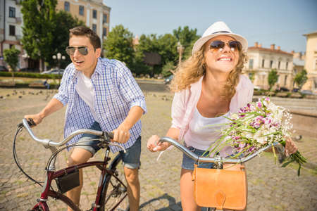 Couple in sunglasses riding on bicycles on the city street and having fun.の写真素材