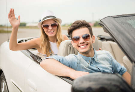Shot outdoors in cabriolet. Young couple friends in sunglasses looking at camera and smiling.の写真素材