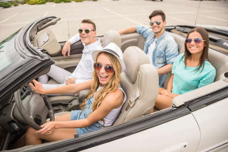 Four happy friends in sunglasses traveling in the cabriolet.の写真素材