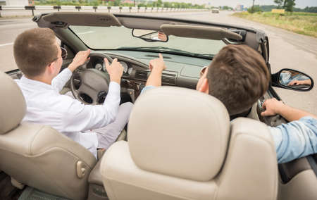 Two young boys driving by cabriolet on the road. Back view.の写真素材