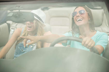Beautiful girls in sunglasses driving on cabriolet, looking away and having fun.の写真素材
