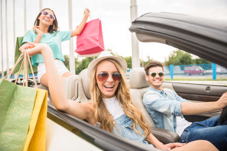 Happy girls returning from store with shopping bags with theirs boyfriend by cabriolet.の写真素材