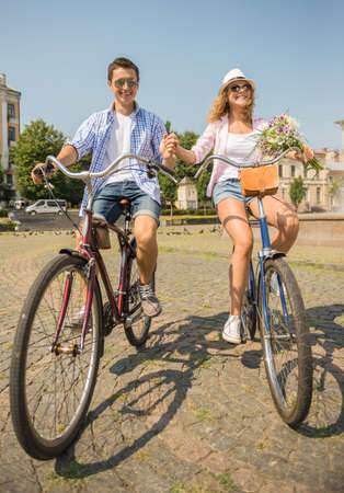 Couple in sunglasses riding on bicycles on the city street and holding hands.の写真素材