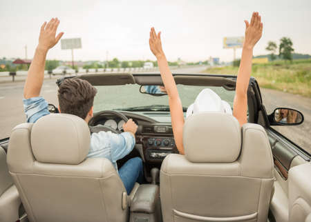 Happy couple traveling on the cabriolet with hands up. Back view.の写真素材