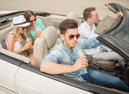 Group of happy friends traveling on the cabriolet and drinking juice.の写真素材