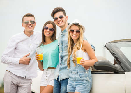 Two happy couples standing near cabriolet and looking at camera. Girls holding glasses of juice.の写真素材