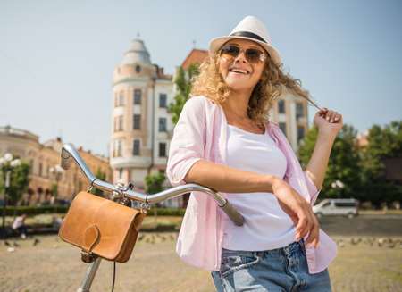 Attractive woman in sunglasses with bicycle on the city street in sunny day.の写真素材
