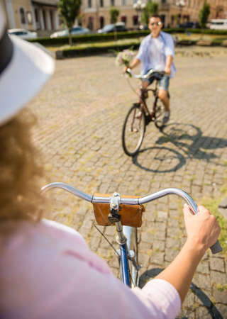Woman in hat and man with flowers riding on bicycles to each other.の写真素材