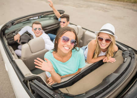 Happy friends sitting in the cabriolet, looking back and smiling at camera.の写真素材