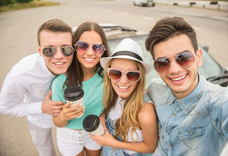 Two beautiful couples near cabriolet looking at camera and smiling. Girls holding cup of coffee.の写真素材
