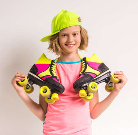 Portrait of smiling girl wearing peaked cap and holding roller skates on her shoulders against white background.の写真素材