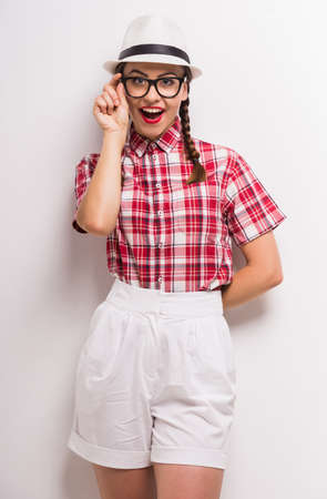 Flirty girl in glasses and hat smiling at camera on white background.の写真素材