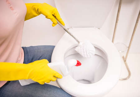Woman with a rubber glove cleans a toilet bowl using means for cleaningの写真素材