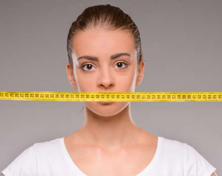 Beautiful young caucasian woman with measure tape on grey background.の写真素材