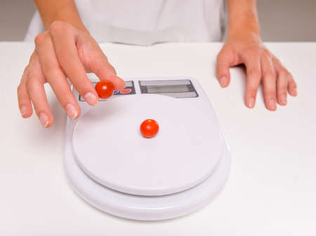 Close-up hands of young woman weighs a tomatoes. Concept of healthy food.の写真素材
