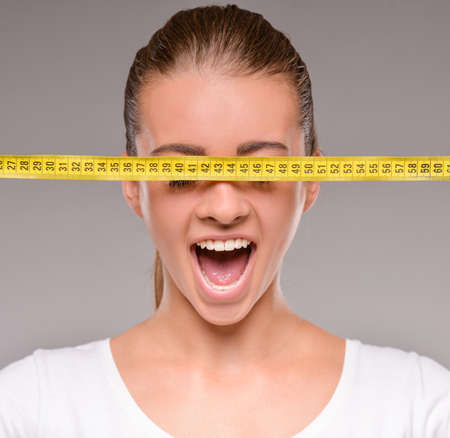 Beautiful young caucasian woman with measure tape on grey background.の写真素材