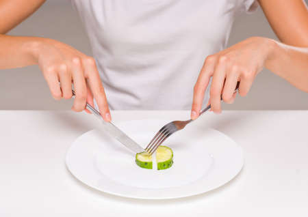 Healthy eating, vegetarian food, dieting. Young woman is eating a cucumber.の写真素材