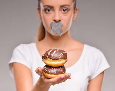 Dieting concept: pretty young woman with chocolate cake and closed mouth by sticky tape.の写真素材